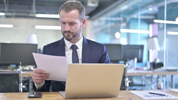 Joven Empresario leyendo Documentos en Office Desk — Vídeos de Stock