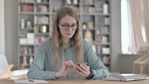 Fiatal Nő diák segítségével okostelefon, miközben ül a tanulószobában — Stock videók