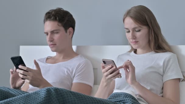 침대에 앉아서 스마트폰을 사용하는 매력적 인 부부 — 비디오