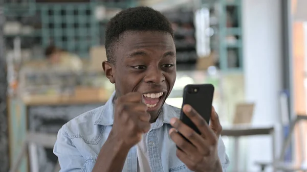 Retrato de un joven africano celebrando el éxito en Smartphone —  Fotos de Stock