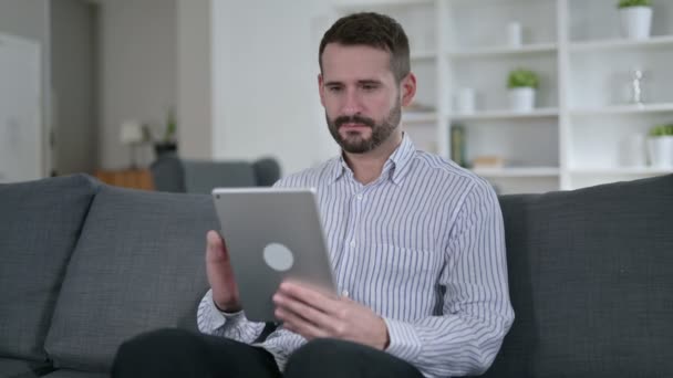Захоплений чоловік святкує успіх на планшеті вдома — стокове відео
