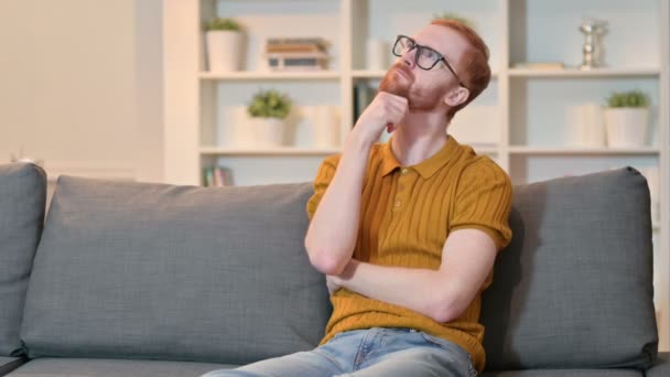 Pensive Redhead άνθρωπος κάθεται στον καναπέ στο σπίτι και τη σκέψη — Αρχείο Βίντεο