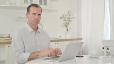 Dizüstü bilgisayarı olan neşeli orta yaşlı adam parmak ile işaret ediyor.