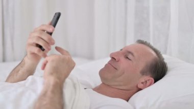 Yatakta akıllı telefon kullanan gevşemiş orta yaşlı adam