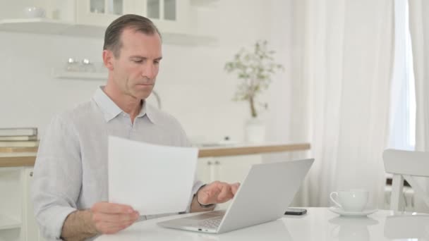 Homem de meia-idade focado trabalhando no laptop e documento em casa — Vídeo de Stock