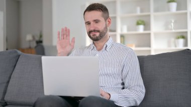 Neşeli Genç Adam evdeki laptopta görüntülü sohbet yapıyor. 