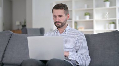 Evde dizüstü bilgisayarda çalışan odaklanmış genç adam. 