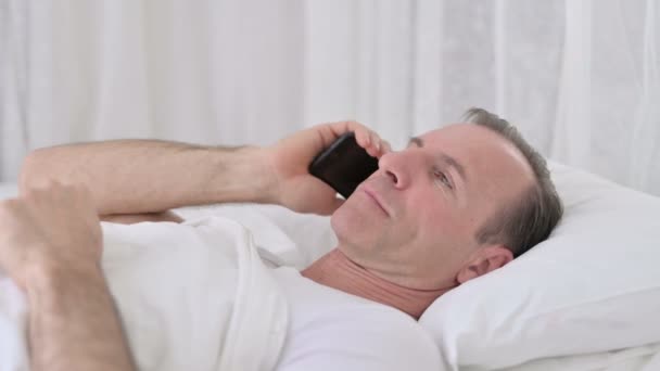 Positivo uomo di mezza età che parla su smartphone a letto — Video Stock