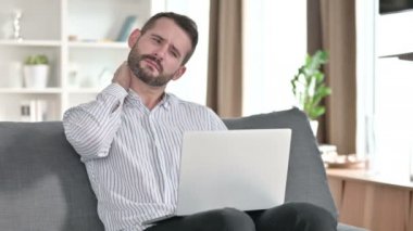 Dizüstü bilgisayarı olan yorgun genç iş adamı evde boyun ağrısı çekiyor. 