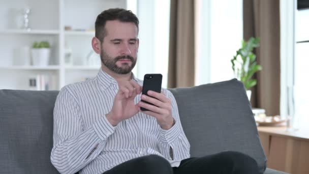 Серьезный молодой бизнесмен, использующий смартфон дома — стоковое видео