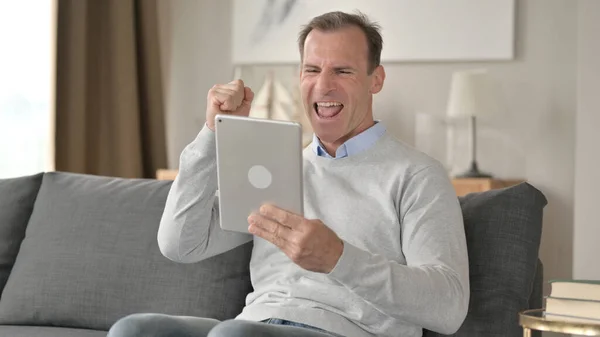 Geschäftsmann mittleren Alters feiert Erfolg auf dem Tablet zu Hause — Stockfoto
