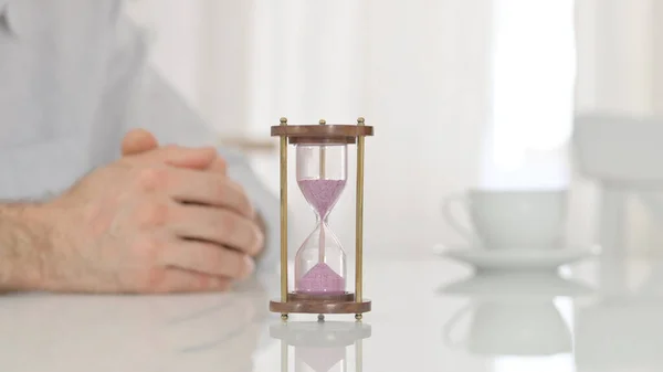 Песочные часы на столе рядом с руками человека, ждущего с нетерпением — стоковое фото