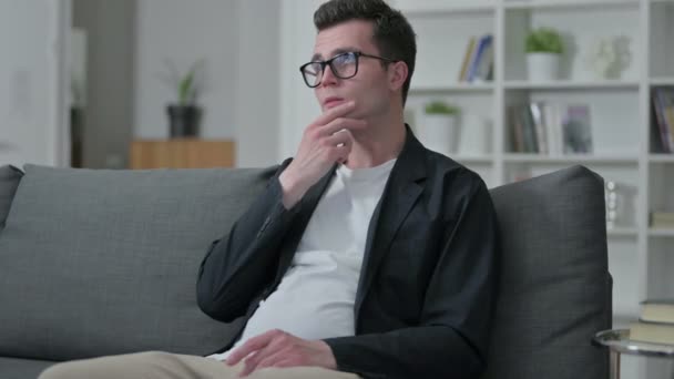 Pensive Mladý muž designér sedí na pohovce a přemýšlí doma — Stock video