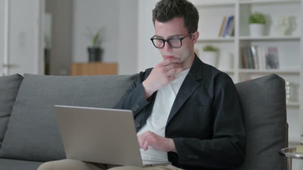 Pensive Mladý muž designér myšlení a práce na notebooku doma — Stock video