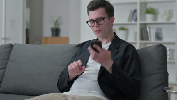 Fröhlicher junger männlicher Designer spricht zu Hause auf dem Smartphone — Stockvideo