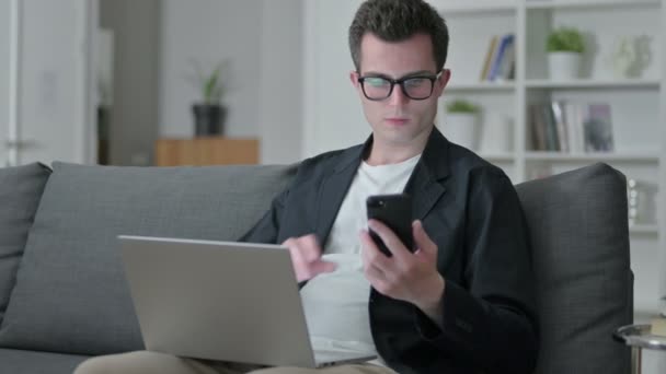 Jonge Man Ontwerper met Laptop Praten op Smartphone thuis — Stockvideo