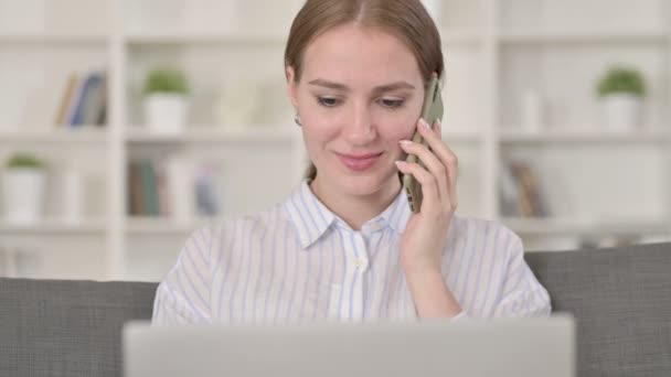 Retrato de mujer joven con el ordenador portátil que habla en el teléfono inteligente — Vídeo de stock