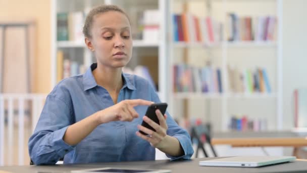 Donna africana seria che utilizza Smartphone in biblioteca — Video Stock