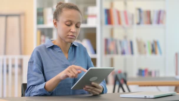 Atractiva mujer africana celebrando el éxito en la tableta en la biblioteca — Vídeos de Stock