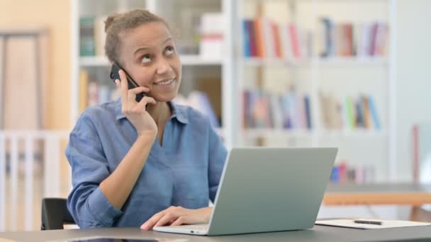 Femme africaine avec ordinateur portable Parler sur Smartphone dans la bibliothèque — Video