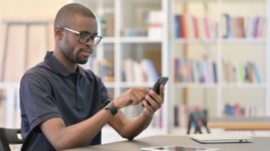 Kütüphanede akıllı telefon kullanan çekici bir Afrikalı.