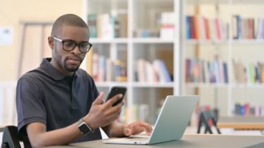 Kütüphanede Smartphone ve Laptop üzerinde çalışan odaklanmış Afrikalı Adam