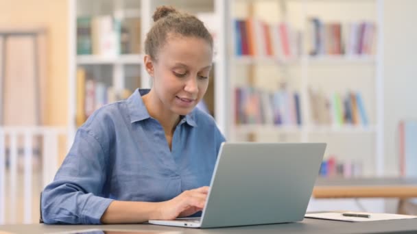 Vrolijke Afrikaanse vrouw werkt op laptop in de bibliotheek — Stockvideo