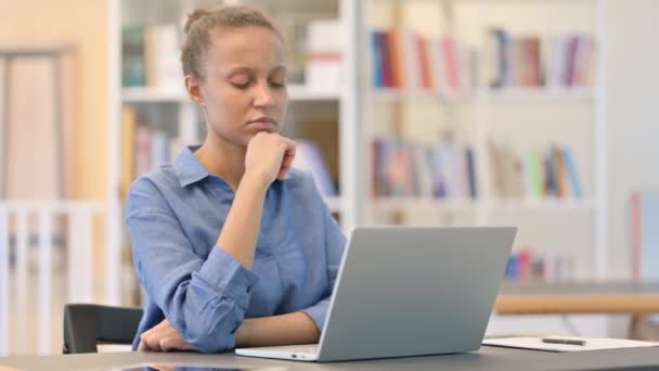 Pensiv afrikansk kvinna tänker och arbetar på laptop i biblioteket — Stockvideo