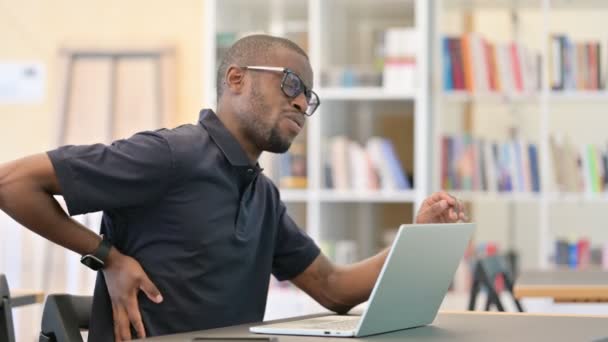 Müder Afrikaner arbeitet in Bibliothek mit Rückenschmerzen am Laptop — Stockvideo