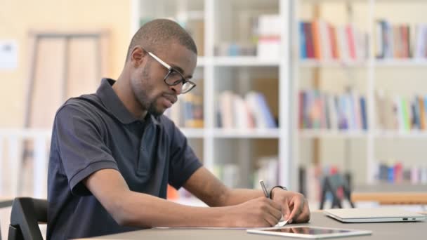 Young African Man denken en doen van papierwerk in de bibliotheek — Stockvideo