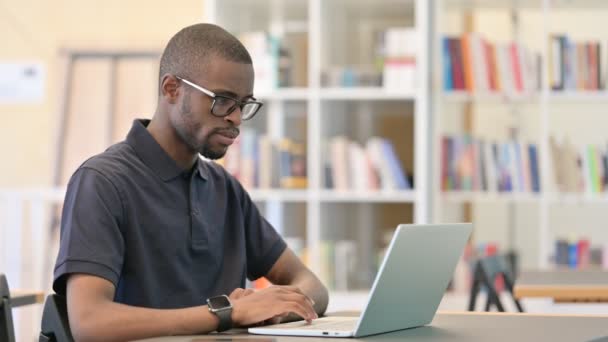 Afrikanischer Mann denkt und arbeitet in Bibliothek am Laptop — Stockvideo