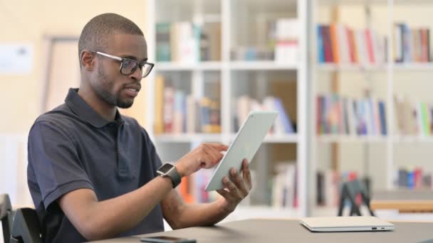 Succes, Jonge Afrikaanse man viert feest op tablet in de bibliotheek — Stockvideo