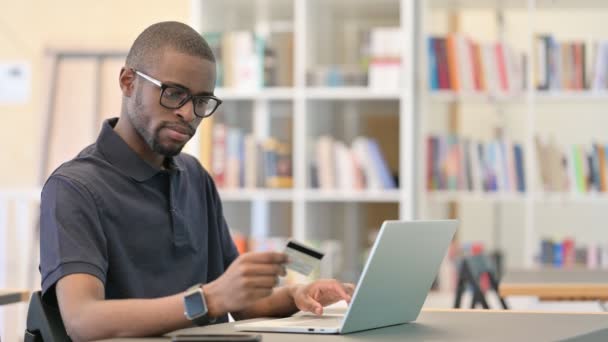 Hombre africano que tiene fallo de pago en línea en el ordenador portátil en la biblioteca — Vídeo de stock