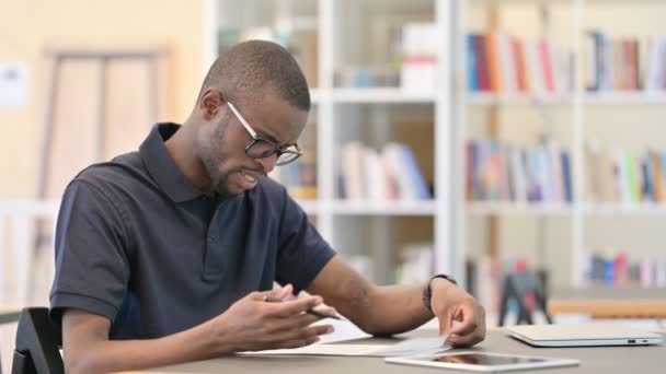 図書館で書類作業をしている失望したアフリカ人青年 — ストック動画