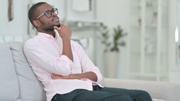 Pensiv ung afrikansk man sitter på soffan och tänker — Stockvideo
