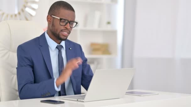 Hombre de negocios africano cansado con el ordenador portátil que tiene dolor de cuello en la oficina — Vídeos de Stock