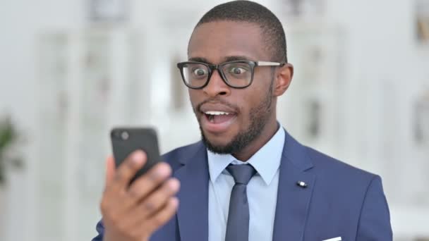 Портрет африканского бизнесмена, празднующего успех на смартфоне — стоковое видео