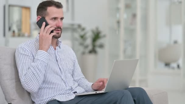 Bilgisayarlı genç adam evde akıllı telefondan konuşuyor. — Stok video