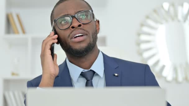 Retrato de hombre de negocios africano con el ordenador portátil hablando en Smartphone — Vídeo de stock