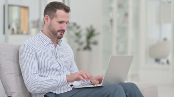 Giovane uomo che celebra il successo sul computer portatile a casa — Video Stock