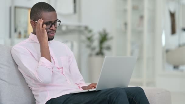 Ung afrikansk man med bärbar dator har huvudvärk hemma — Stockvideo