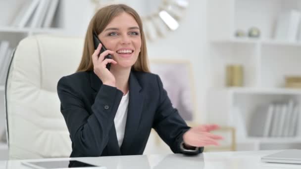 Fröhliche Geschäftsfrau spricht im Büro mit Smartphone — Stockvideo