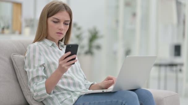 Mujer joven usando teléfono inteligente y portátil en casa — Vídeos de Stock