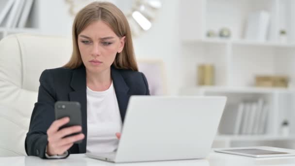 Зайнята ділова жінка за допомогою смартфона і лаптопа в офісі — стокове відео