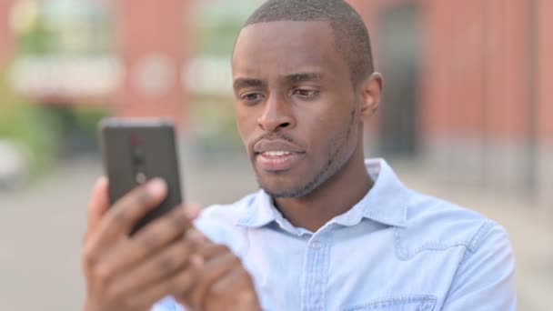 Retrato ao ar livre do homem africano perturbado com perda no smartphone — Vídeo de Stock