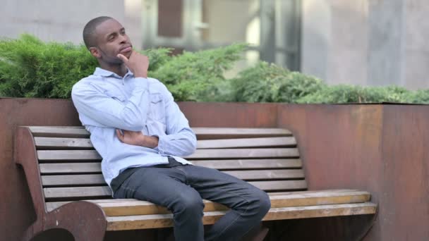 Pensativo joven africano sentado en el banco y pensando — Vídeos de Stock