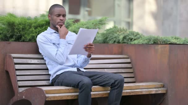 Uomo africano pensieroso che pensa mentre legge i documenti, all'aperto — Video Stock