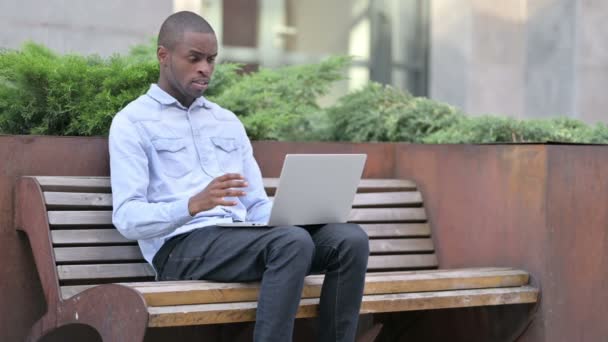 Perturbado hombre africano reaccionando a la pérdida en el ordenador portátil al aire libre — Vídeos de Stock
