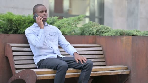 Приваблива африканська людина розмовляє на смартфоні на відкритому повітрі — стокове відео