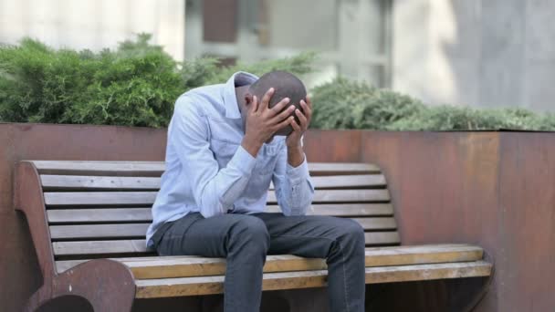 Aggódó fiatal afrikai férfi ül a szabadban, és gondolkodás — Stock videók